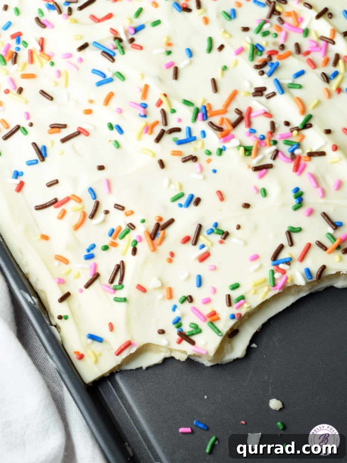 Irresistible Sugar Cookie Bark 3 Close-up of a baking sheet filled with freshly made chocolate bark topped with colorful sprinkles, before being broken into pieces.