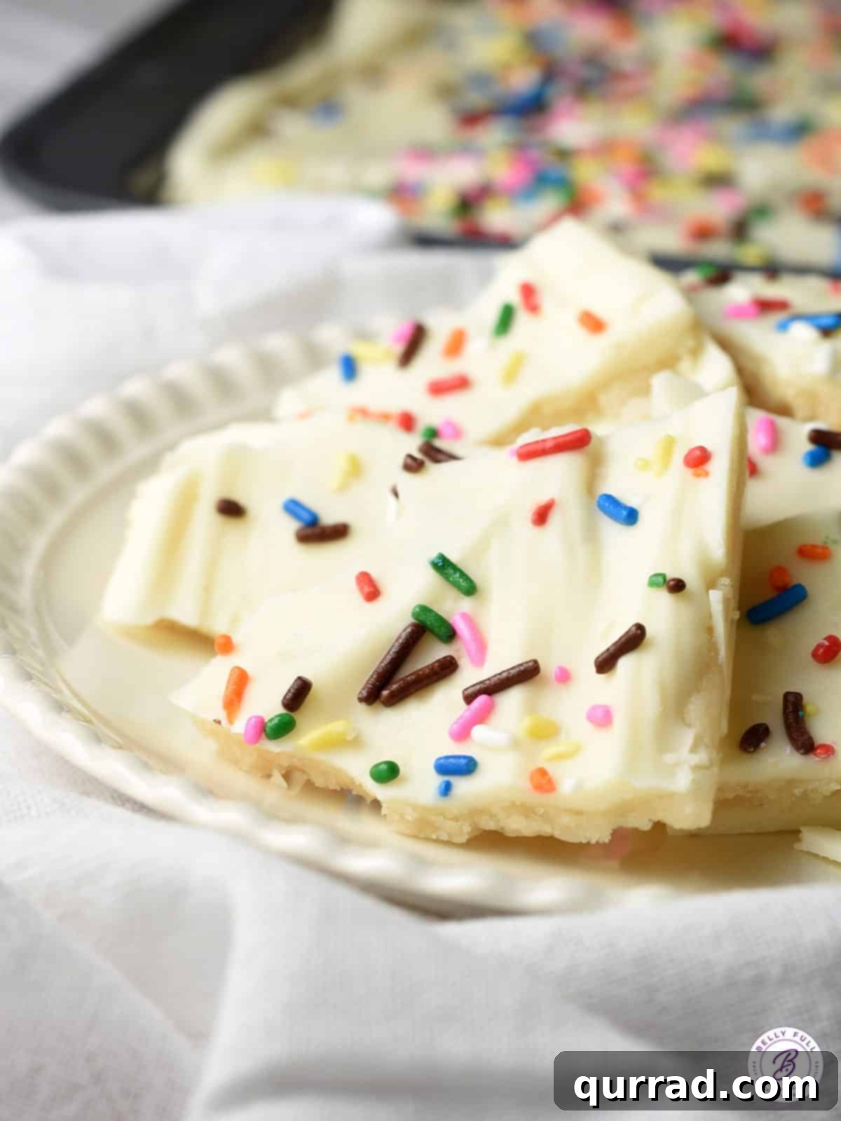 Irresistible Sugar Cookie Bark 4 Various pieces of Sugar Cookie Chocolate Bark on a white plate, showcasing the distinct layers and colorful sprinkles.