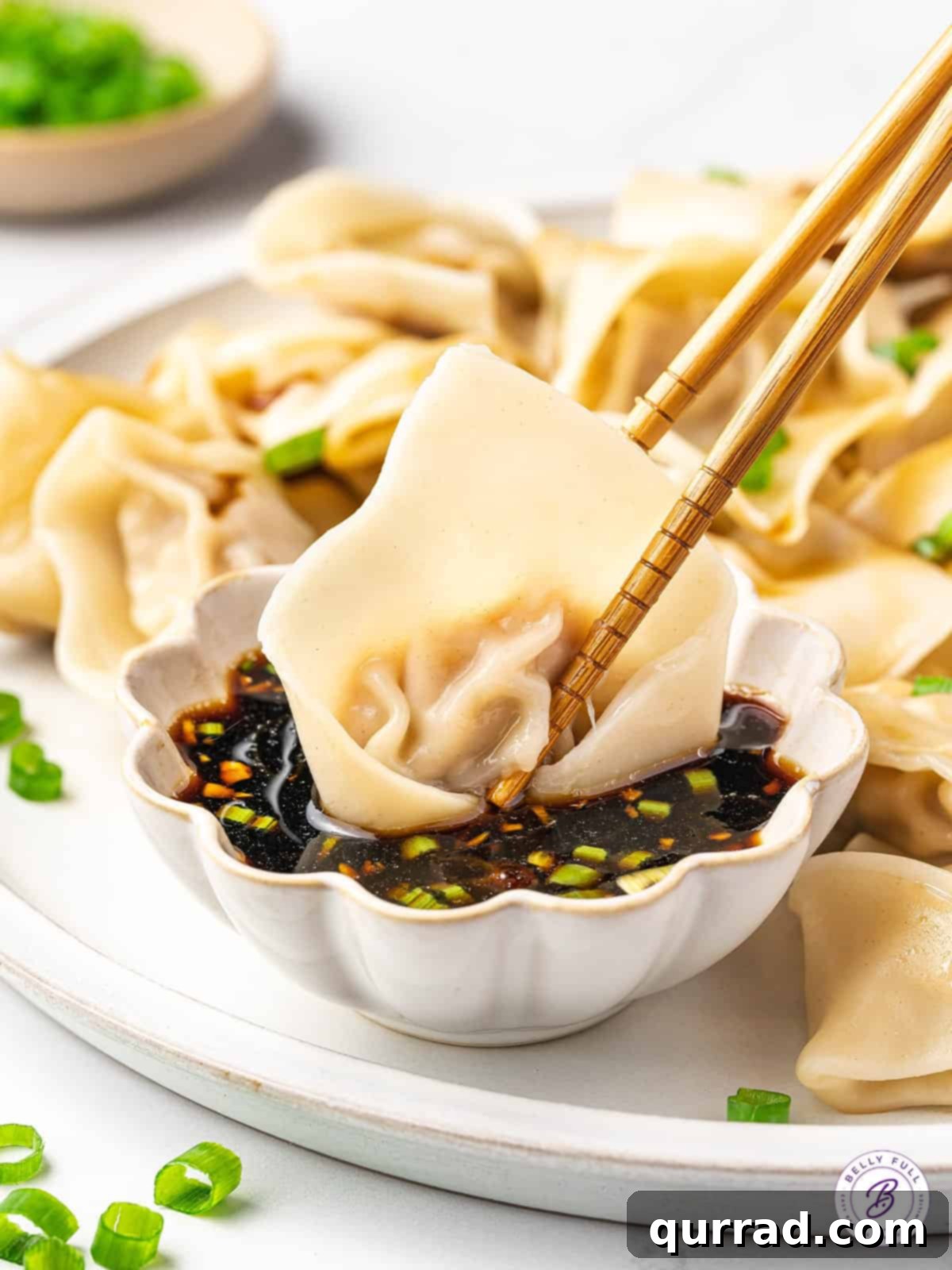 A pair of chopsticks dunking a pork wonton into a small bowl of dipping sauce
