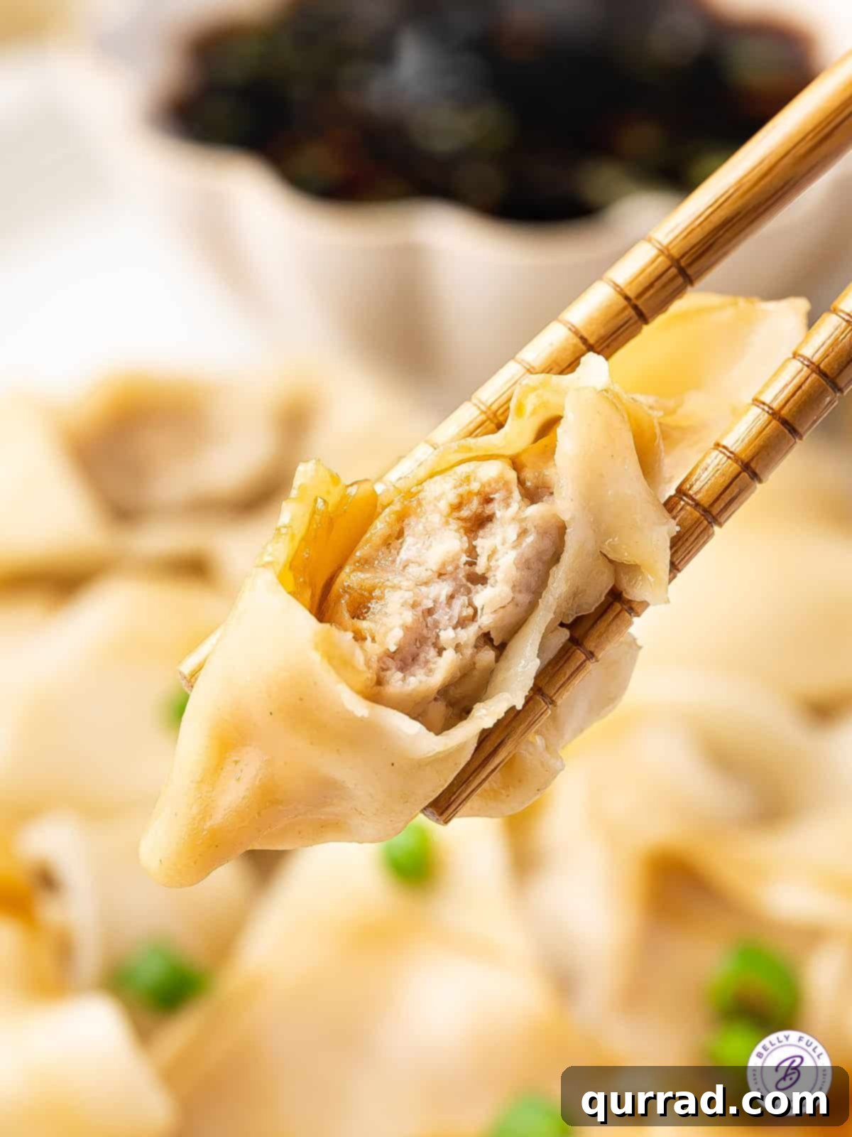 Chopsticks holding a cooked pork wonton, showing the juicy filling inside
