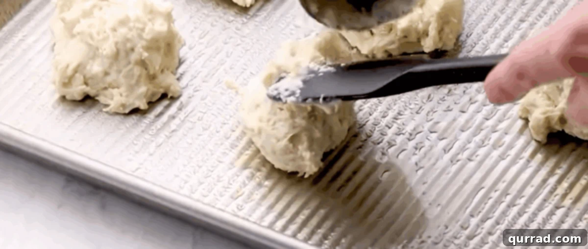 Fluffy Drop Biscuits Smothered in Rich Sausage Gravy 5 A hand dropping portions of sticky biscuit dough onto a greased baking sheet, preparing them for baking to become golden, fluffy biscuits.