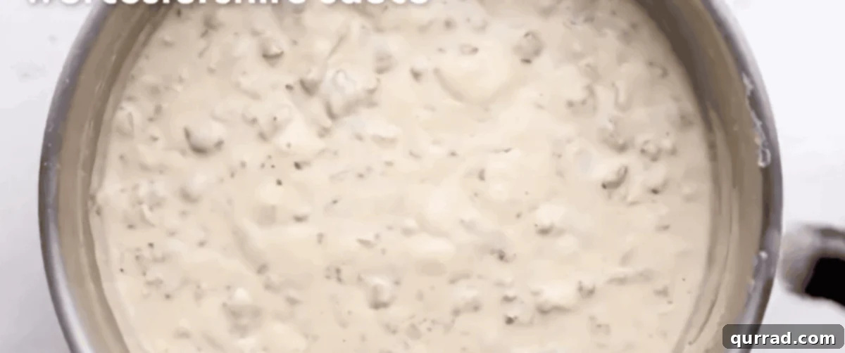 Fluffy Drop Biscuits Smothered in Rich Sausage Gravy 7 A wooden spoon stirring a creamy, thick sausage gravy in a large skillet, showing the perfect texture and consistency for Biscuits and Gravy.