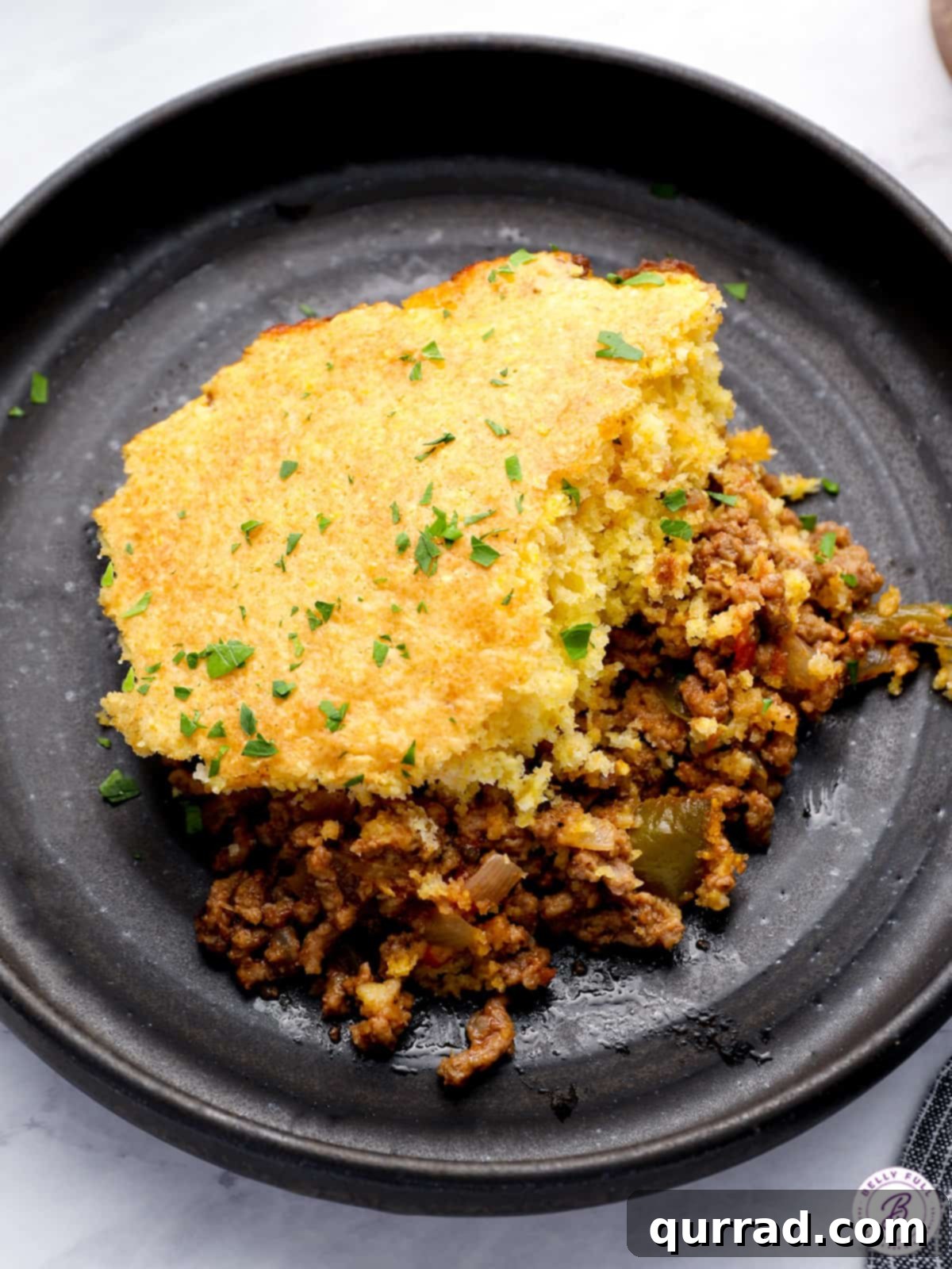 Golden Cornbread Sloppy Joe Pie 2 Hearty serving of cornbread sloppy joe skillet on a plate with fresh parsley, highlighting the golden cornbread topping over the rich meat mixture.