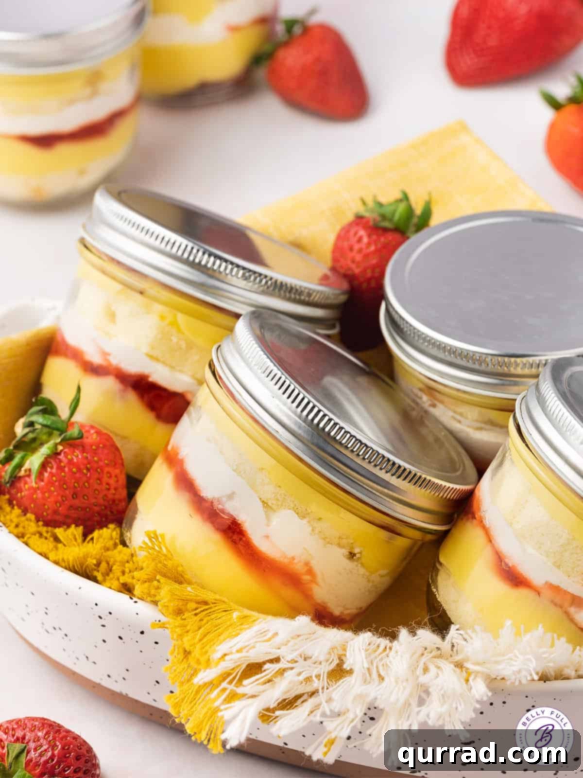 Strawberry Shortcake Layers of Sweetness 3 Four charming strawberry shortcake parfaits in glass jars with lids, nestled in a woven basket