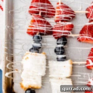 overhead dessert kabobs on baking sheet made with blueberries, strawberries, and angel food cake, drizzled with white chocolate
