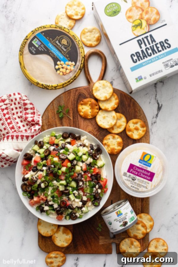 Vibrant Mediterranean Layered Dip 5 Overhead view of a beautifully prepared Greek Layered Dip, showcasing the vibrant colors of its Mediterranean ingredients including cream cheese, hummus, olives, cucumber, and tomato