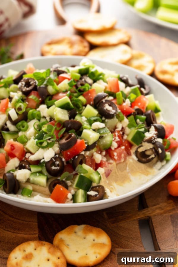 Vibrant Mediterranean Layered Dip 7 Elegant white ceramic dish filled with a finished Greek Layered Dip, ready for serving with dippers