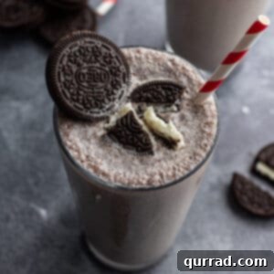Oreo milkshake in soda fountain glass with crushed oreos and a red and white striped straw