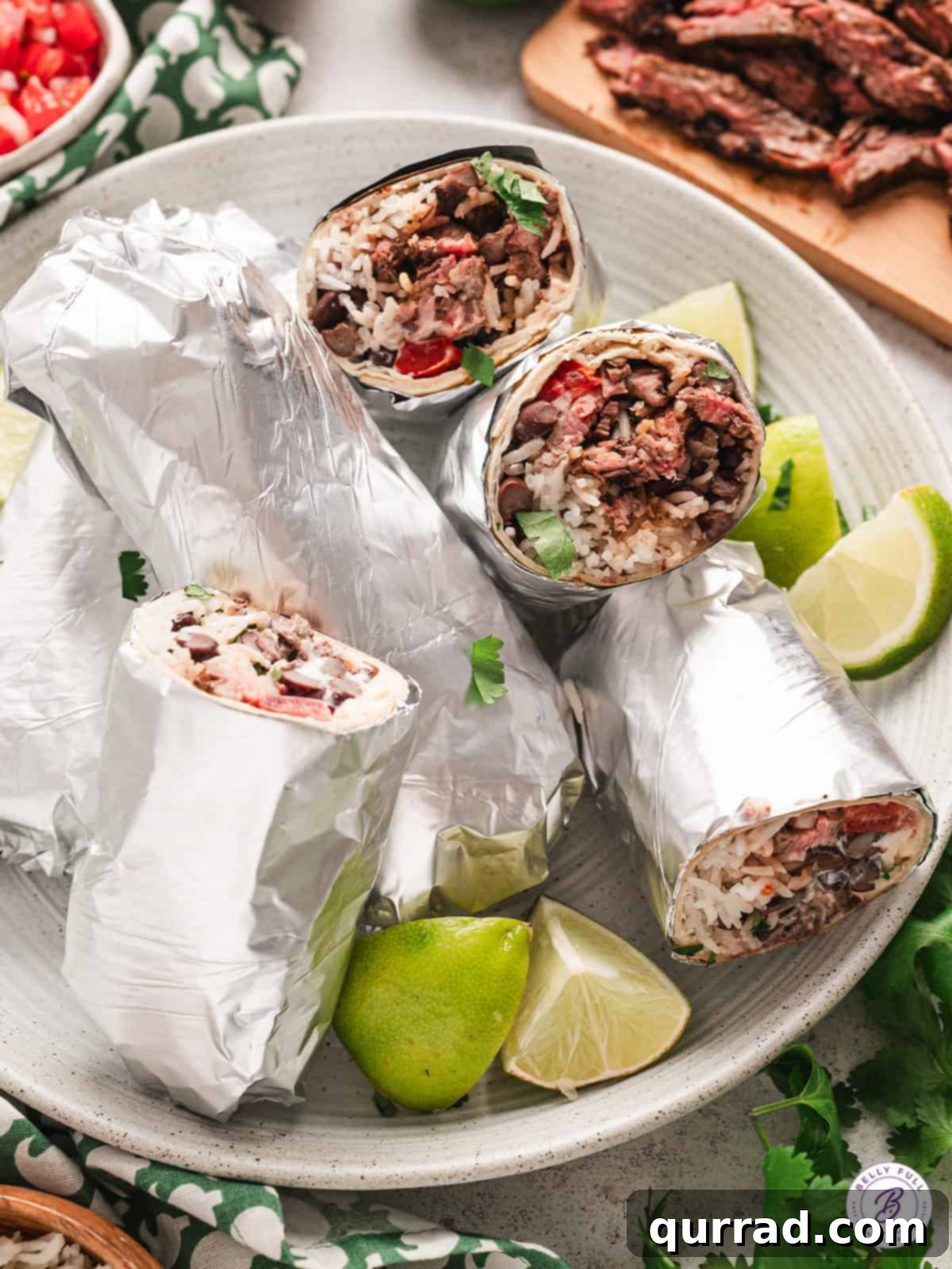 Restaurant-Quality Chipotle Steak Burrito at Home 12 chipotle steak burritos wrapped in foil on plate with lime wedges