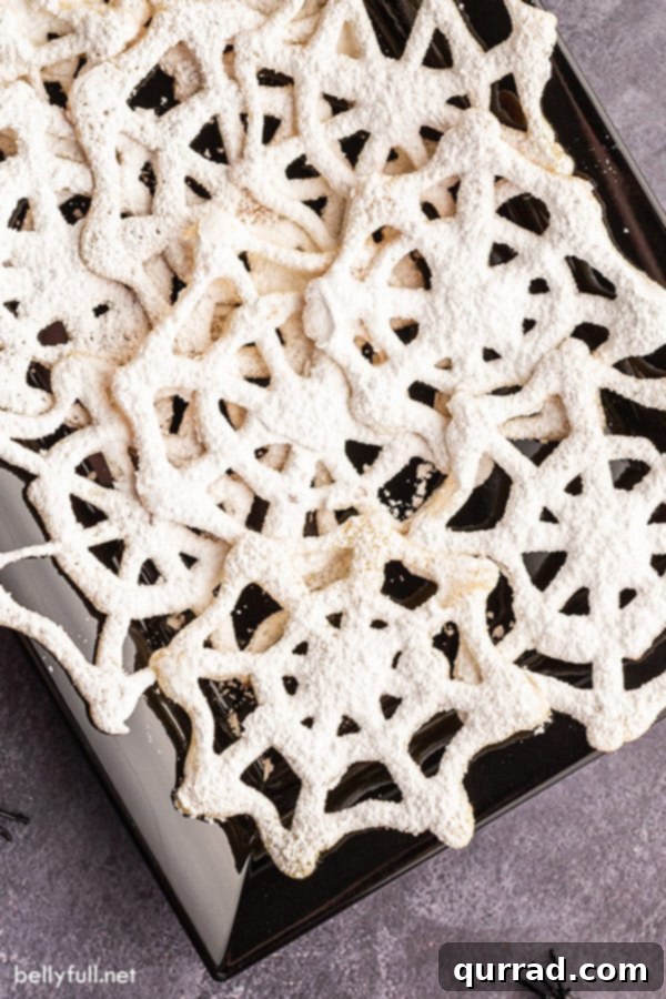 Spooky Spiderweb Delights 2 Close-up overhead view of a black serving tray generously filled with golden-brown spiderweb cookies, dusted with powdered sugar.