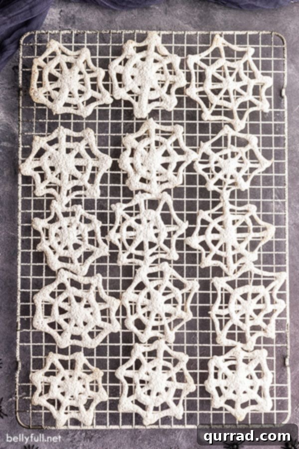 Spooky Spiderweb Delights 3 An overhead shot showcasing fifteen freshly baked cobweb cookies cooling on a wire rack, ready for dusting.