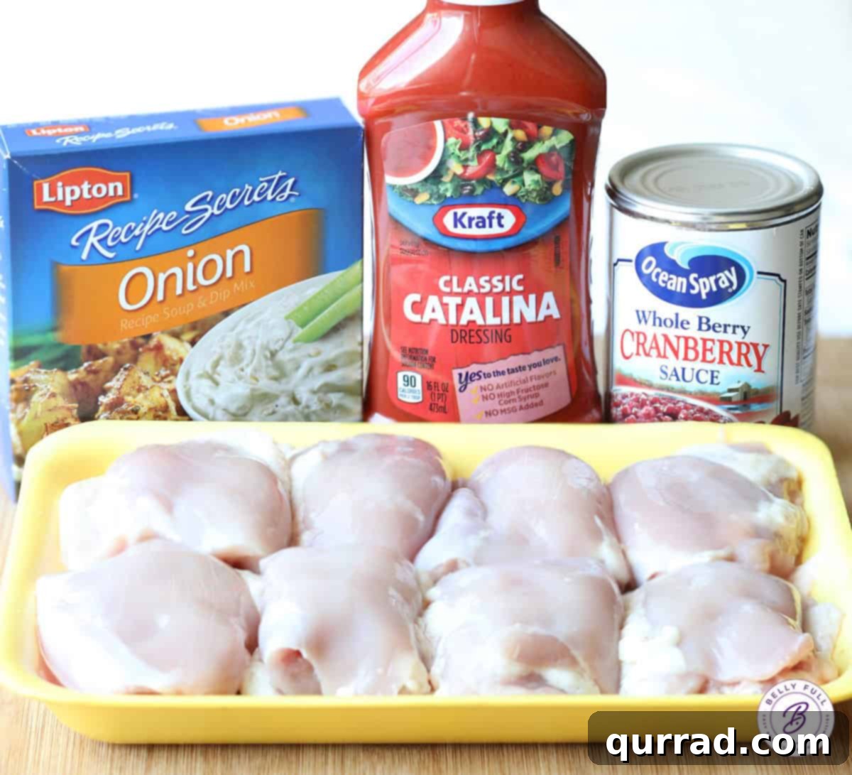 Cranberry Glazed Chicken 4 A vibrant display of fresh ingredients laid out on a kitchen counter, including boneless, skinless chicken thighs, a bottle of Catalina dressing, a packet of dry onion soup mix, and a can of whole-berry cranberry sauce.