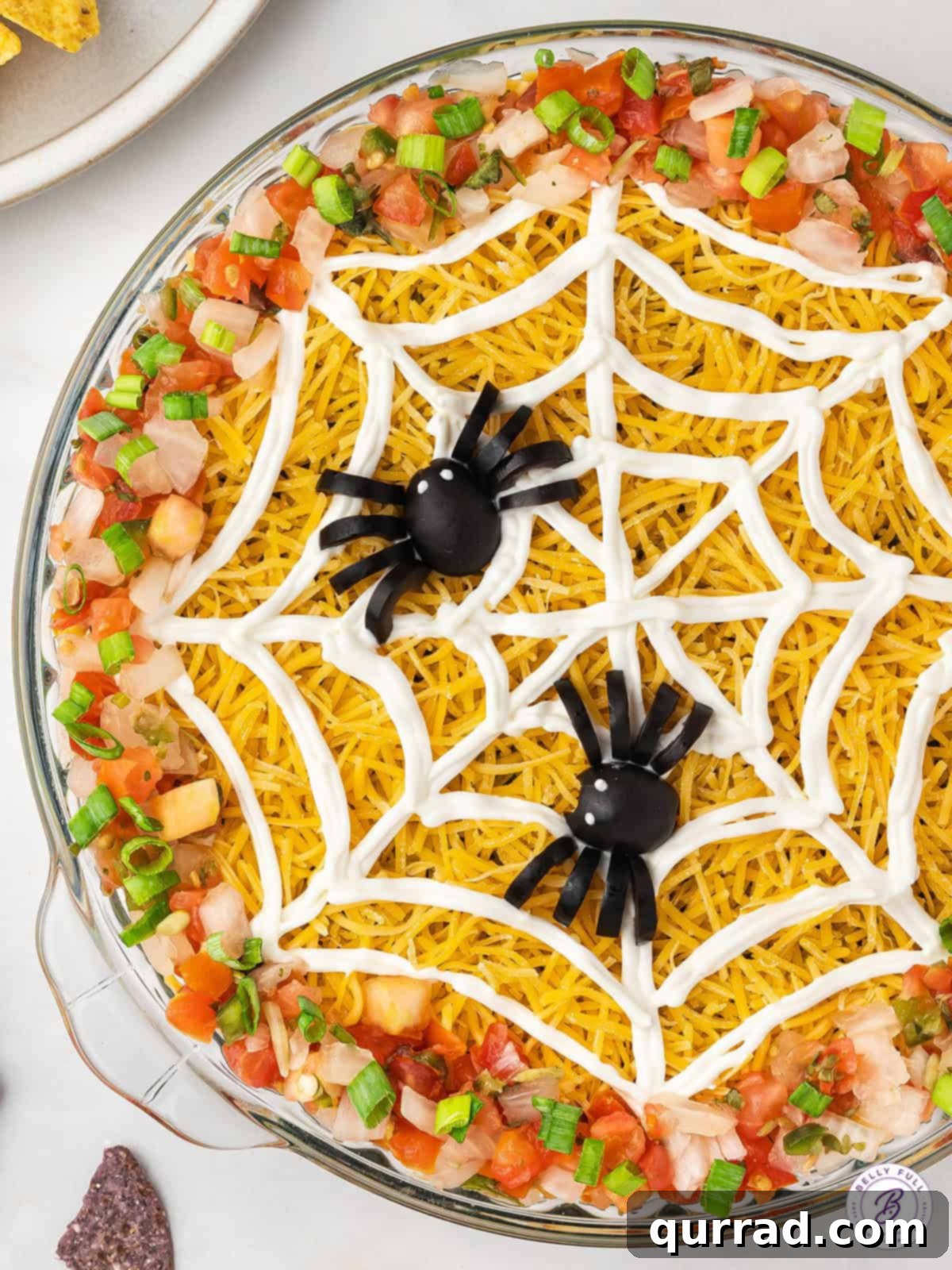 Wicked Web Dip 2 Close-up overhead view of a festive Halloween Spiderweb Dip, adorned with black olive spiders, served in a round dish with colorful tortilla chips.