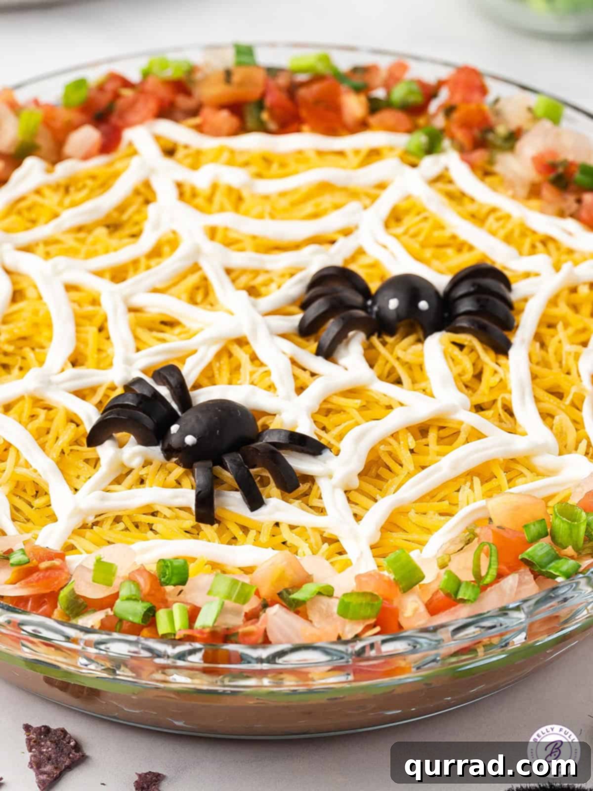 Wicked Web Dip 3 Detailed close-up of a black olive spider crawling on a sour cream spiderweb, showcasing the intricate Halloween decoration of the dip.