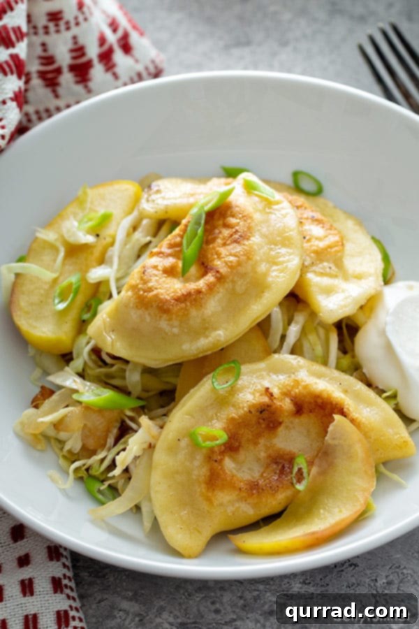 A close-up view of several golden, pan-fried pierogi nestled amidst a colorful mix of sautéed cabbage and apple slices in a rustic bowl, ready to be enjoyed.