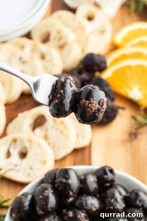 Fig Balsamic Infused Olives 4 Close-up shot of a marinated black olive on a fork, showcasing its plump texture and glistening marinade.