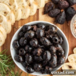 overhead of marinated black olives in white dish surrounded by crostini