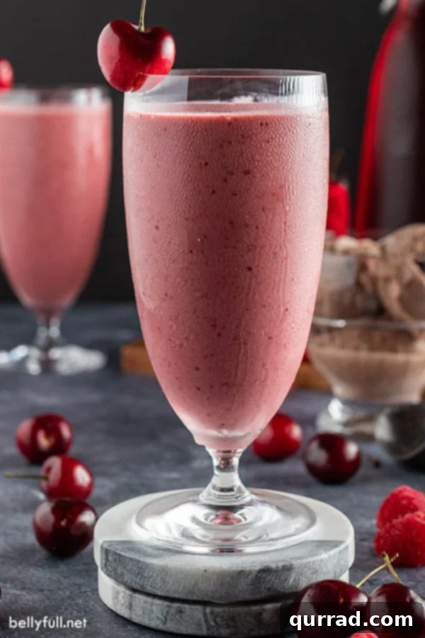 Black Forest Smoothie 2 Tall cold glass filled with a rich chocolate cherry smoothie, garnished with a fresh cherry on top.
