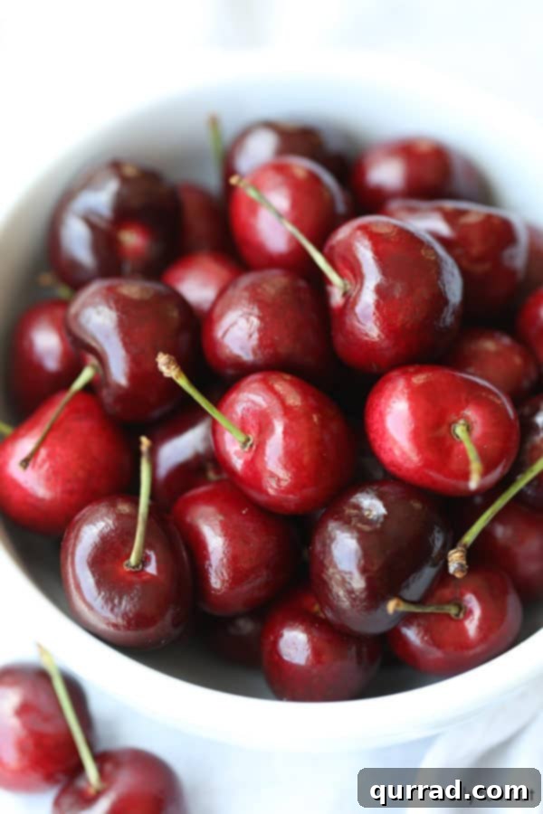 Black Forest Smoothie 3 White bowl brimming with fresh, ripe stemmed cherries, ready for pitting.