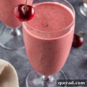 Overhead shot of a tall glass filled with a decadent cherry smoothie, garnished with a fresh cherry on the rim.
