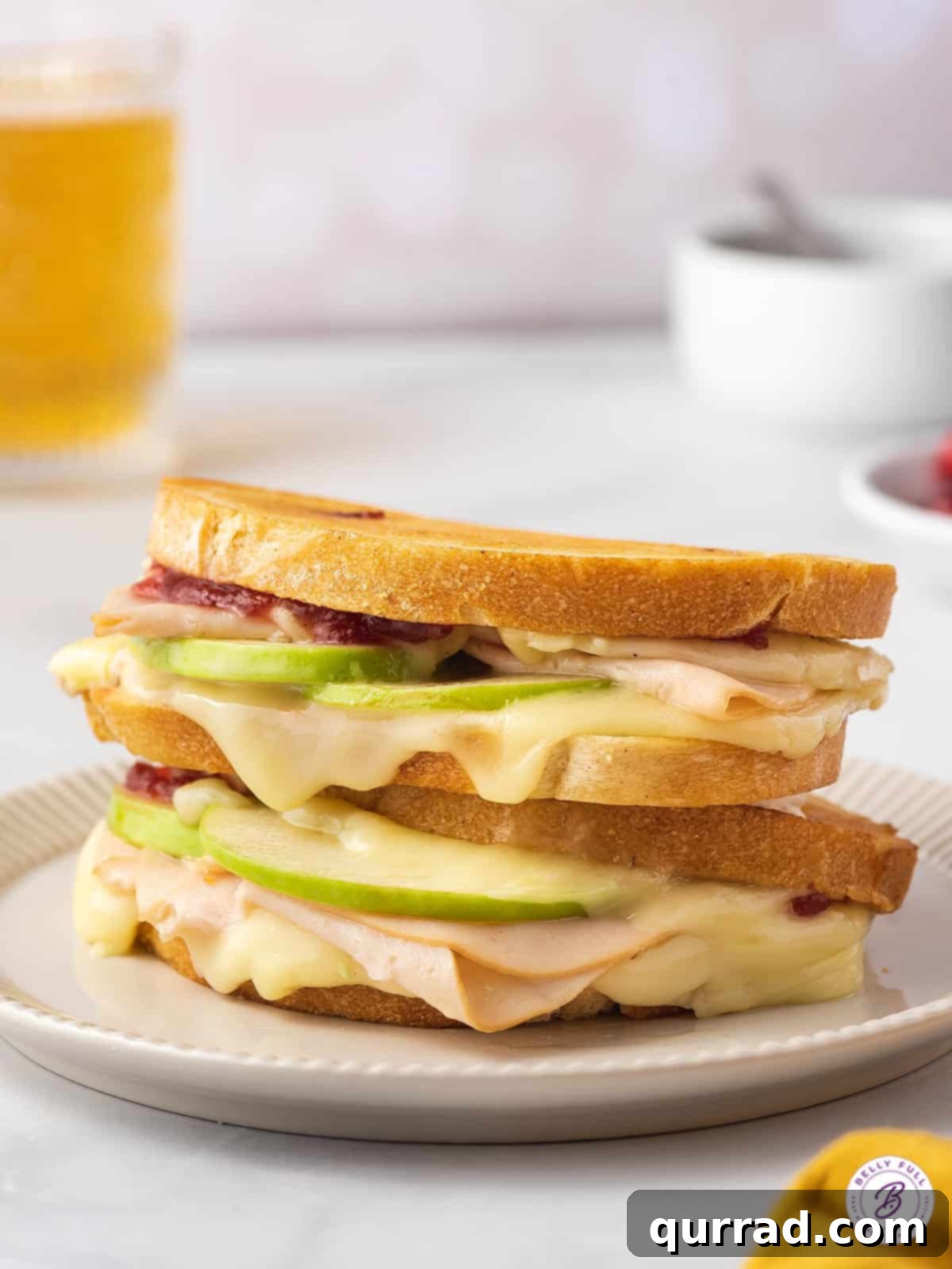 Thanksgiving Leftovers Reinvented 6 Two golden-brown turkey brie grilled cheese sandwiches, perfectly stacked, showcasing melted cheese and a hint of green apple.