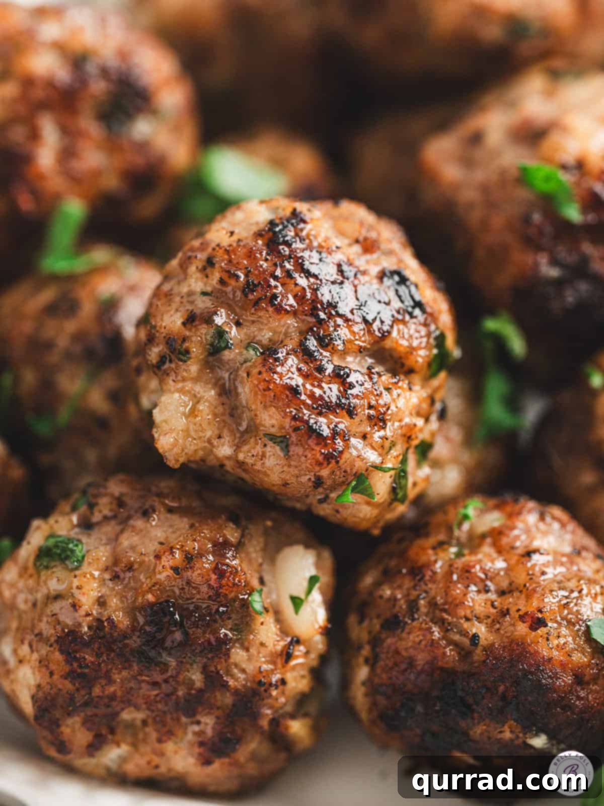 A close-up shot of perfectly cooked, succulent Italian beef meatballs, garnished with fresh herbs.