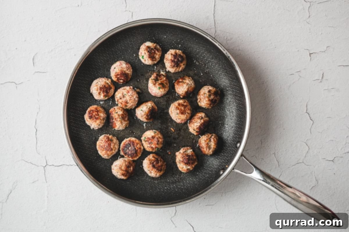 Several homemade Italian Meatballs browning beautifully in a hot skillet with olive oil.