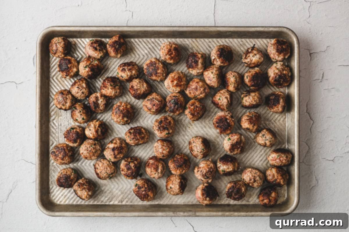 Golden-brown, pan-fried Italian Meatballs arranged in a single layer on a baking sheet, ready for the oven.