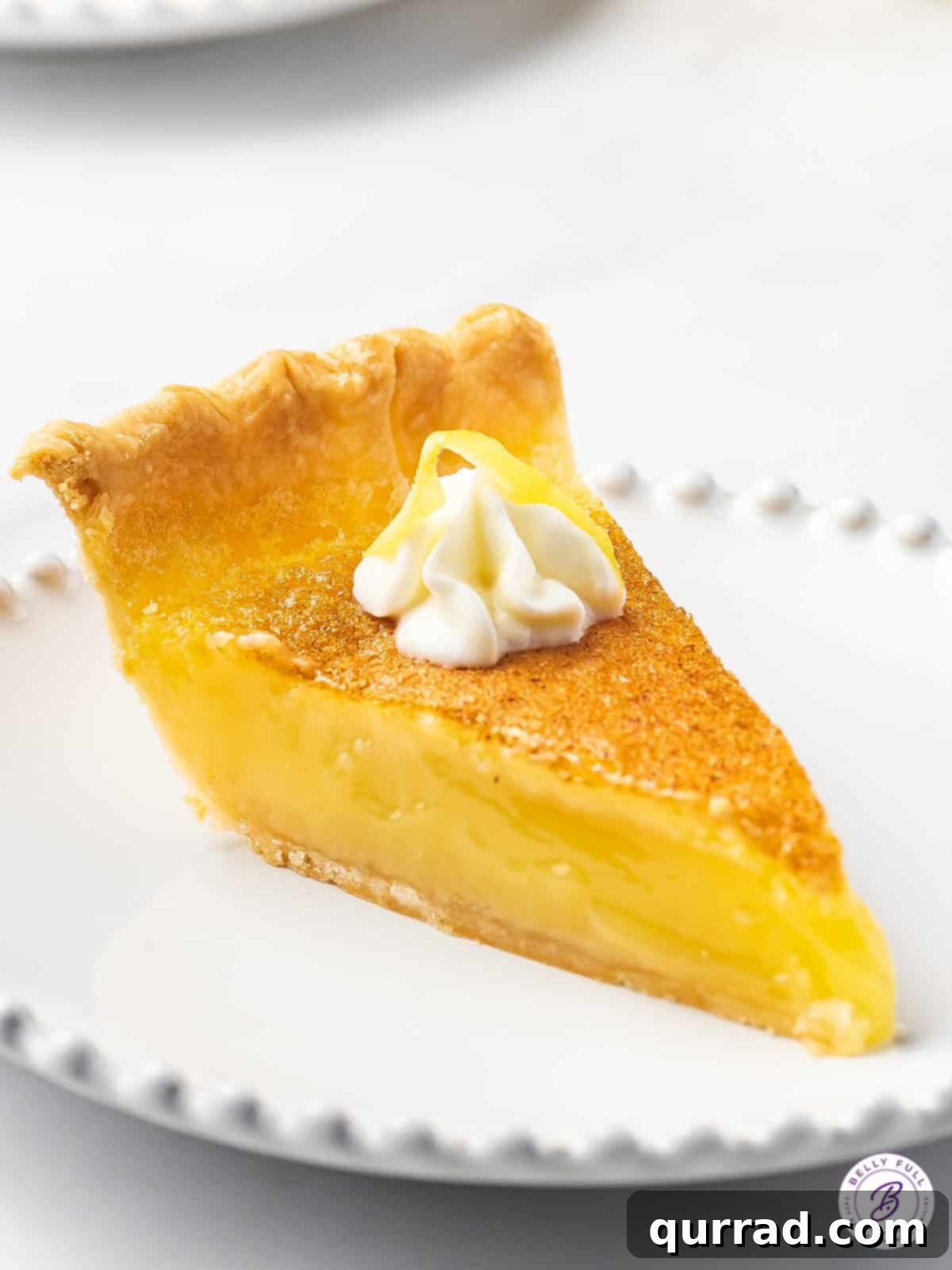 A perfectly portioned slice of bright yellow Lemon Curd Pie on a pristine white plate, ready to be enjoyed.