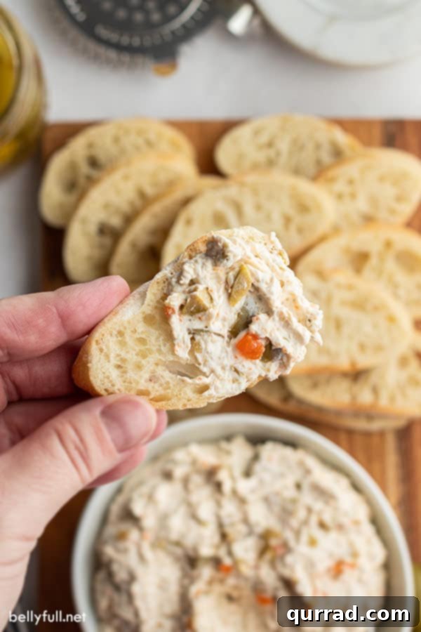Two-Ingredient Olive Tapenade 4 Close up of a hand holding a piece of bread topped with creamy olive dip