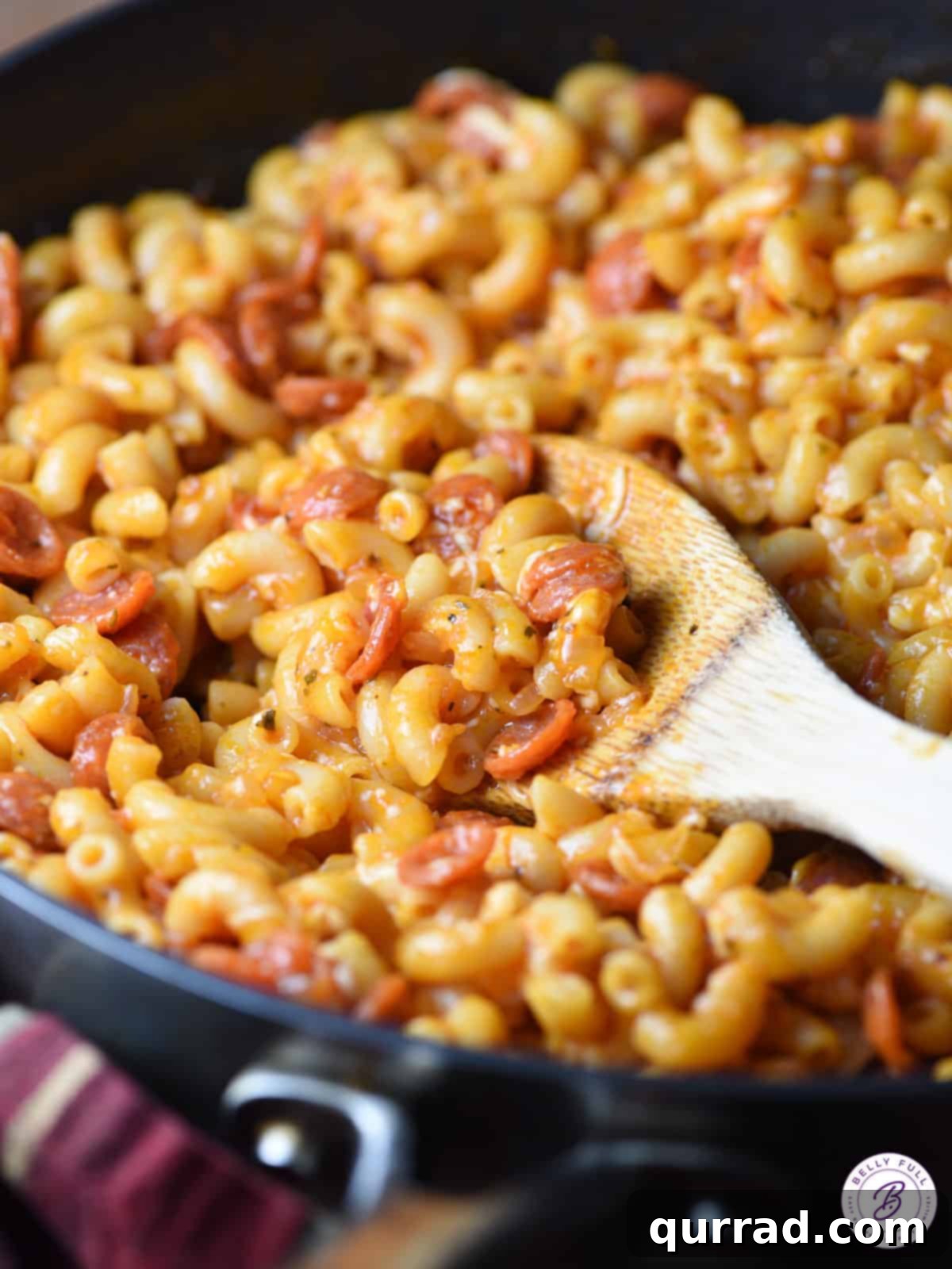 Pizzaroni Mac and Cheese 2 A serving of Pepperoni Pizza Macaroni and Cheese on a rustic wooden spoon, showcasing melted cheese and savory pepperoni pieces.