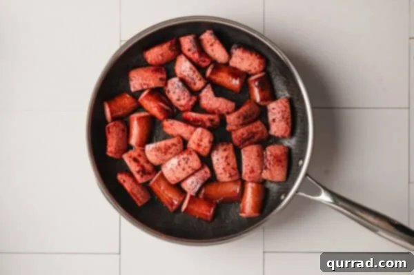Overhead view of fried pieces of kielbasa browning in a skillet.