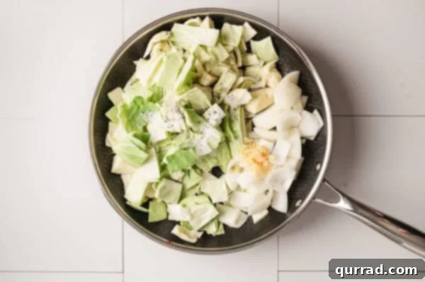 Overhead view of uncooked chopped cabbage, onions, and minced garlic in a skillet.