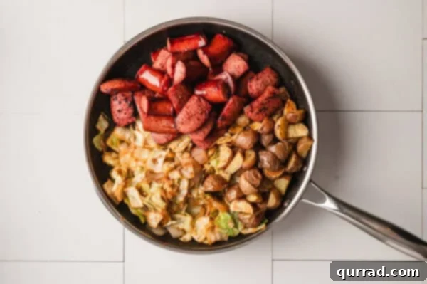 Overhead view of fried kielbasa, cabbage, and roasted potatoes combining in a skillet.