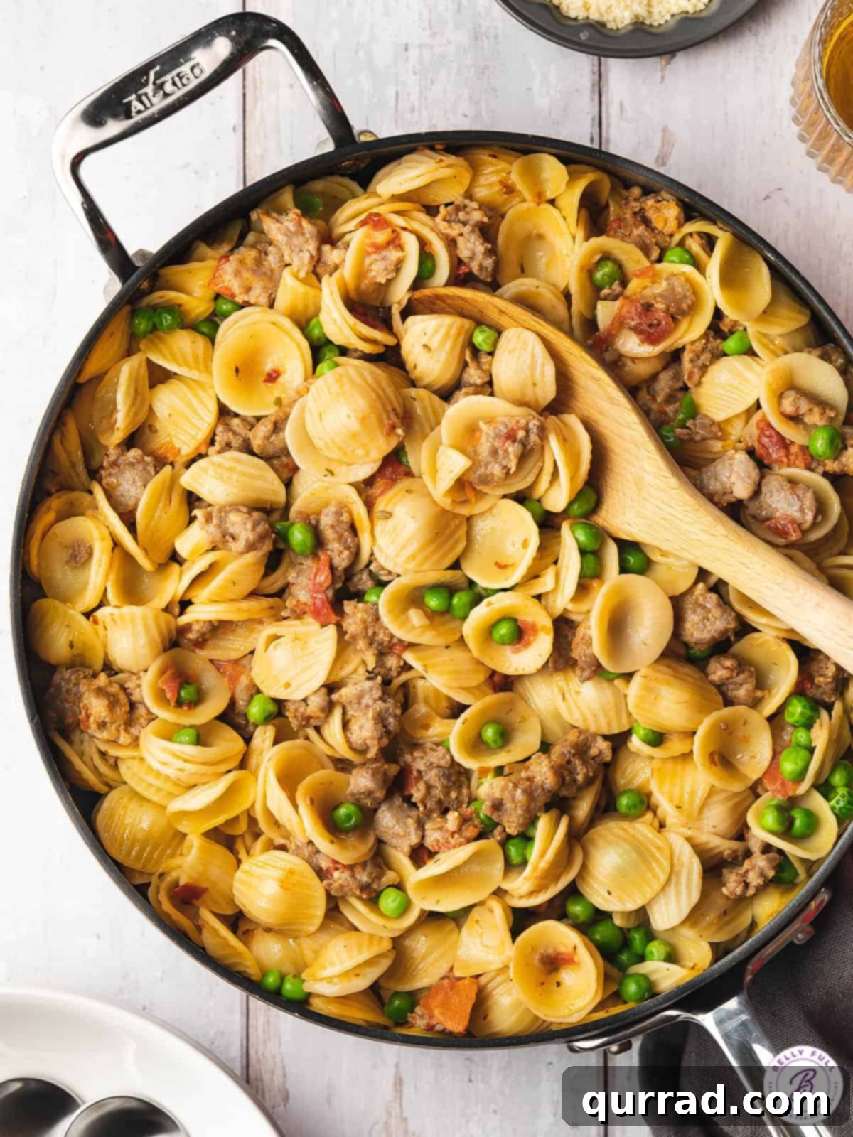 Overhead view of sausage and pea pasta in a skillet with a serving spoon, showcasing its rich texture and vibrant colors.