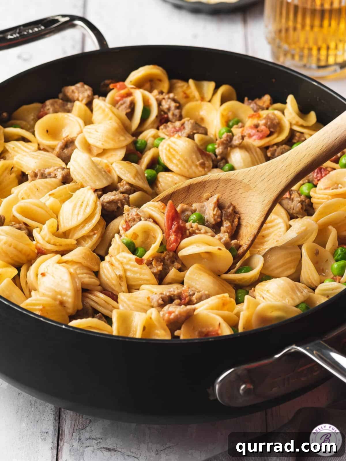 Close-up of orecchiette pasta with crumbled sausage and green peas in a skillet, ready to be served.