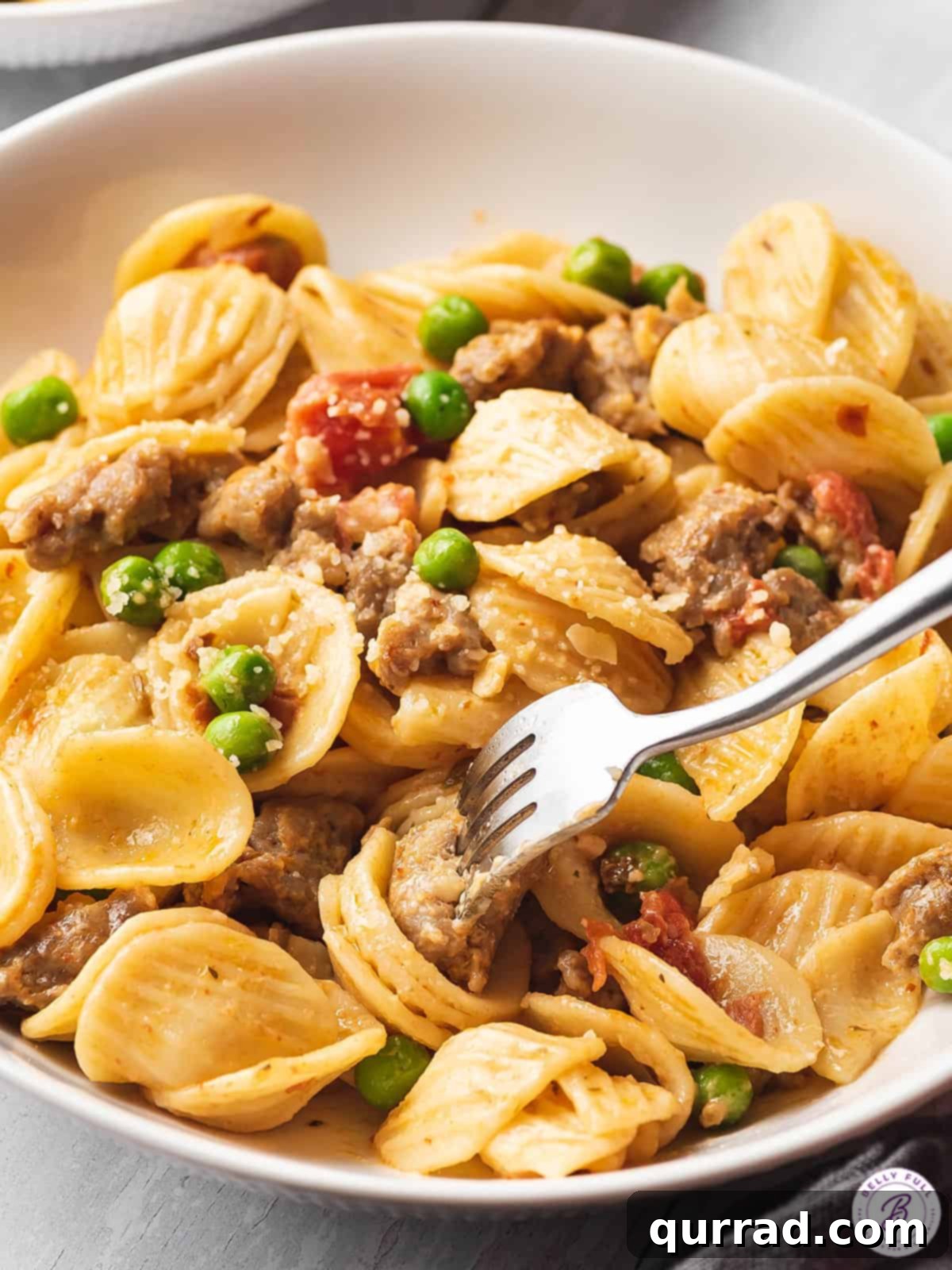 Close-up of orecchiette pasta with sausage and peas in a bowl, ready to be eaten with a fork.