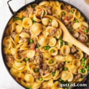Overhead view of sausage and pea pasta in a skillet with a serving spoon