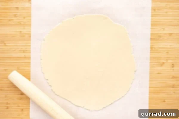 pie crust dough rolled out with rolling pin on parchment paper