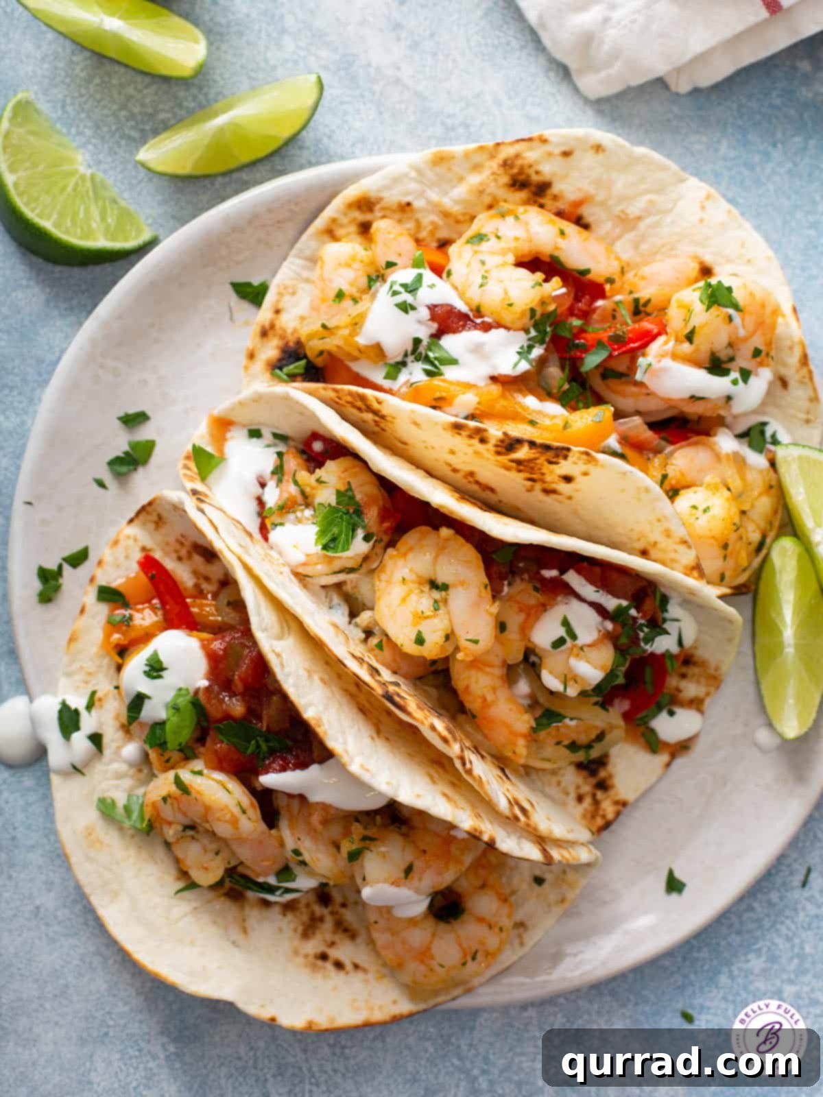 Sizzling Shrimp Fajitas 8 Three assembled shrimp fajitas on a white plate, garnished with fresh cilantro and lime wedges.