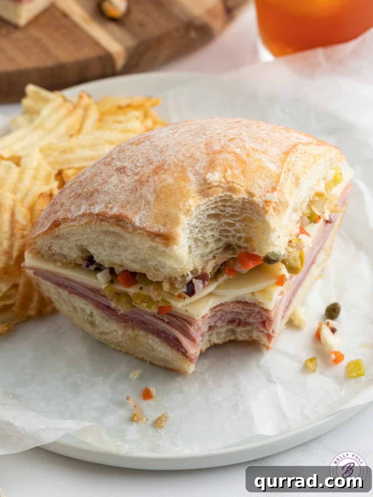 A sliced Muffuletta sandwich served on a plate with potato chips, showing its intricate layers.