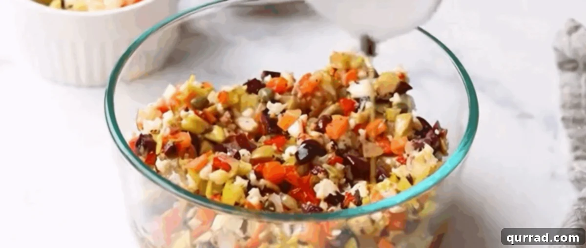 A glass container filled with a vibrant, diced olive salad, marinating in oil.