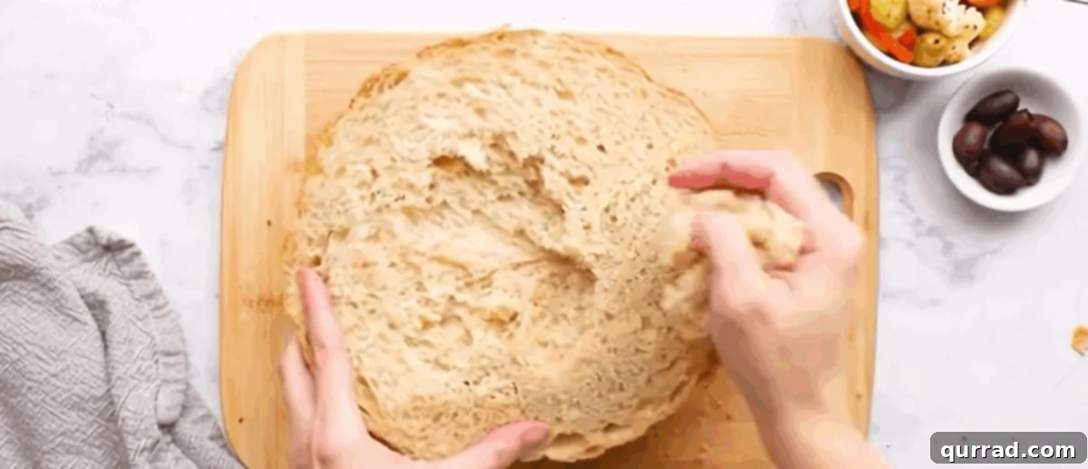 An Italian bread loaf cut in half, with hands gently removing some of the interior bread from the top half to make space for the generous filling.