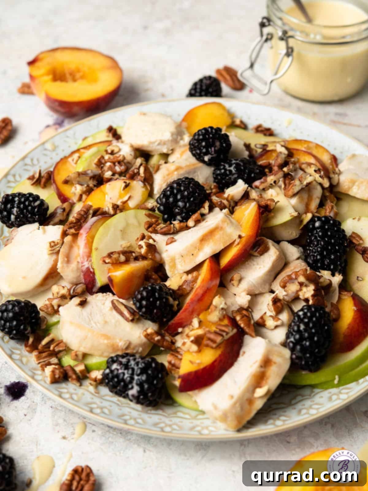 Golden Sesame Chicken Greens 4 Close-up of chicken and fruit being combined in a large bowl, showing blackberries, sliced peaches, and grilled chicken pieces.