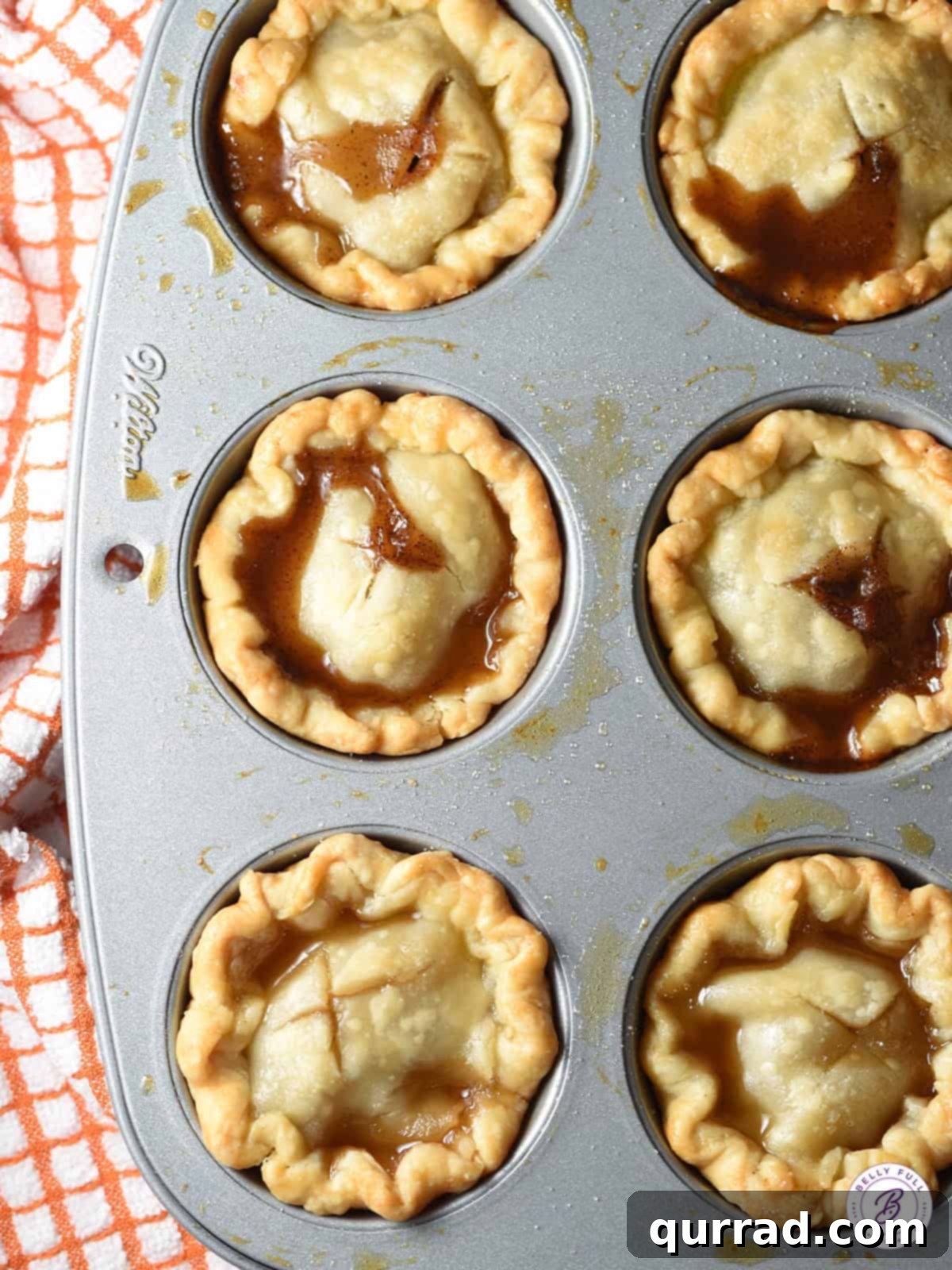 Bite-Sized Peach Delights 2 Overhead view of freshly baked mini peach pies arranged in a mini muffin tin, highlighting their golden crusts and a hint of sweet peach filling.