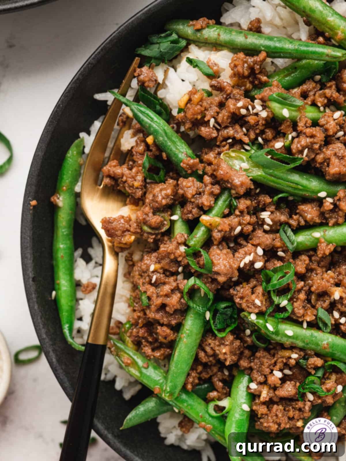 A bowl filled with savory Korean ground beef and vibrant green beans served over fluffy white rice, garnished with sesame seeds.