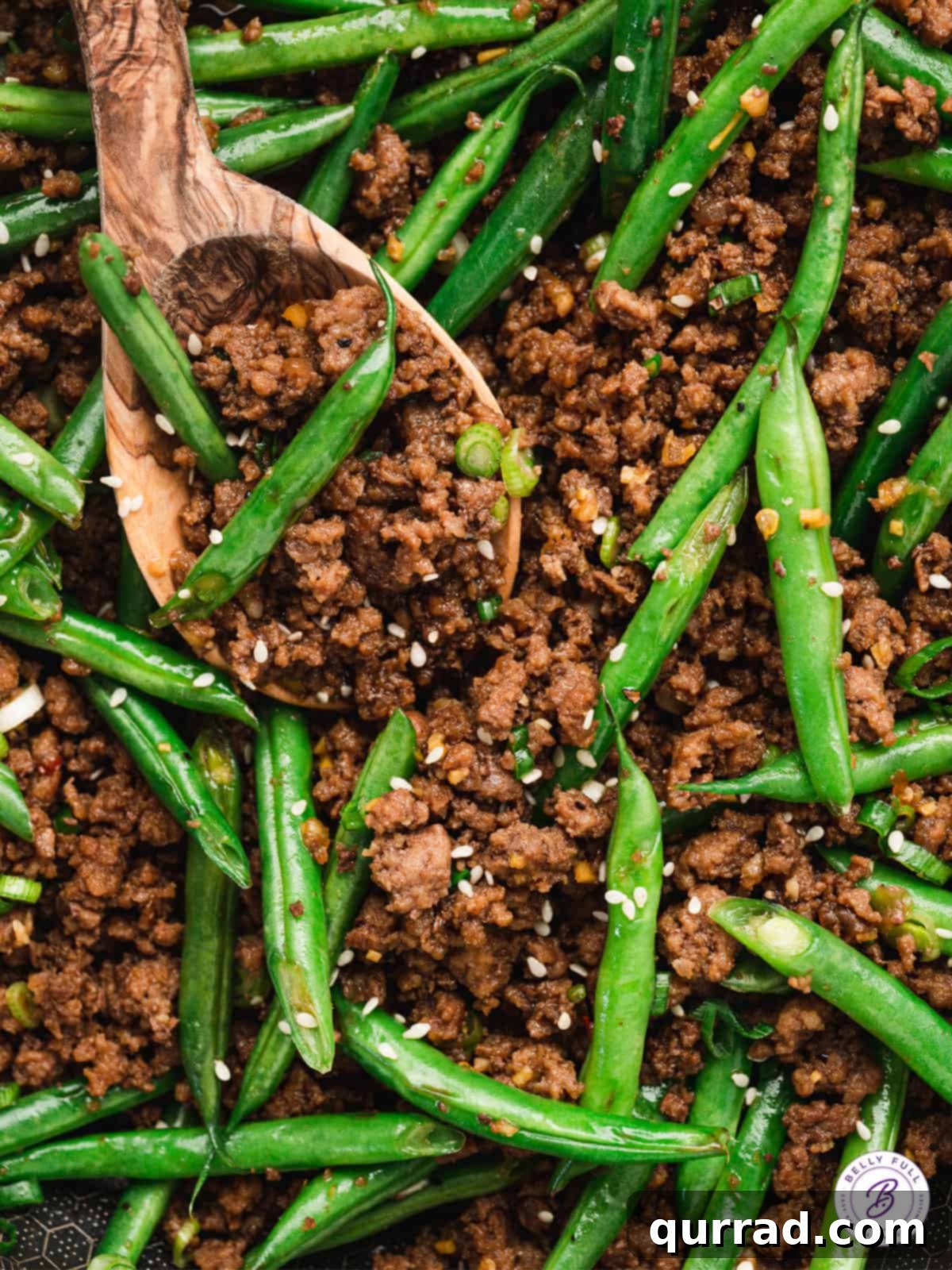 Close-up of savory BBQ ground beef mixed with green beans, served with a wooden spoon for serving.