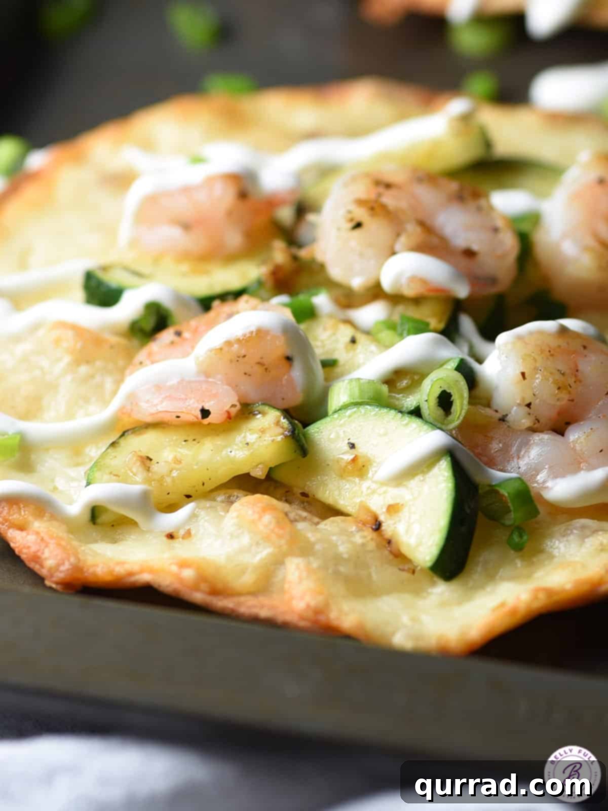 Zesty Shrimp & Zucchini Tostadas 3 Close-up of a single shrimp and zucchini tostada on a wooden board, topped with sour cream.