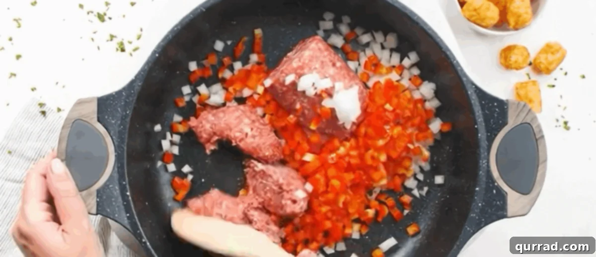 Sausage, diced onions, and bell peppers cooking in a nonstick skillet, browning beautifully.