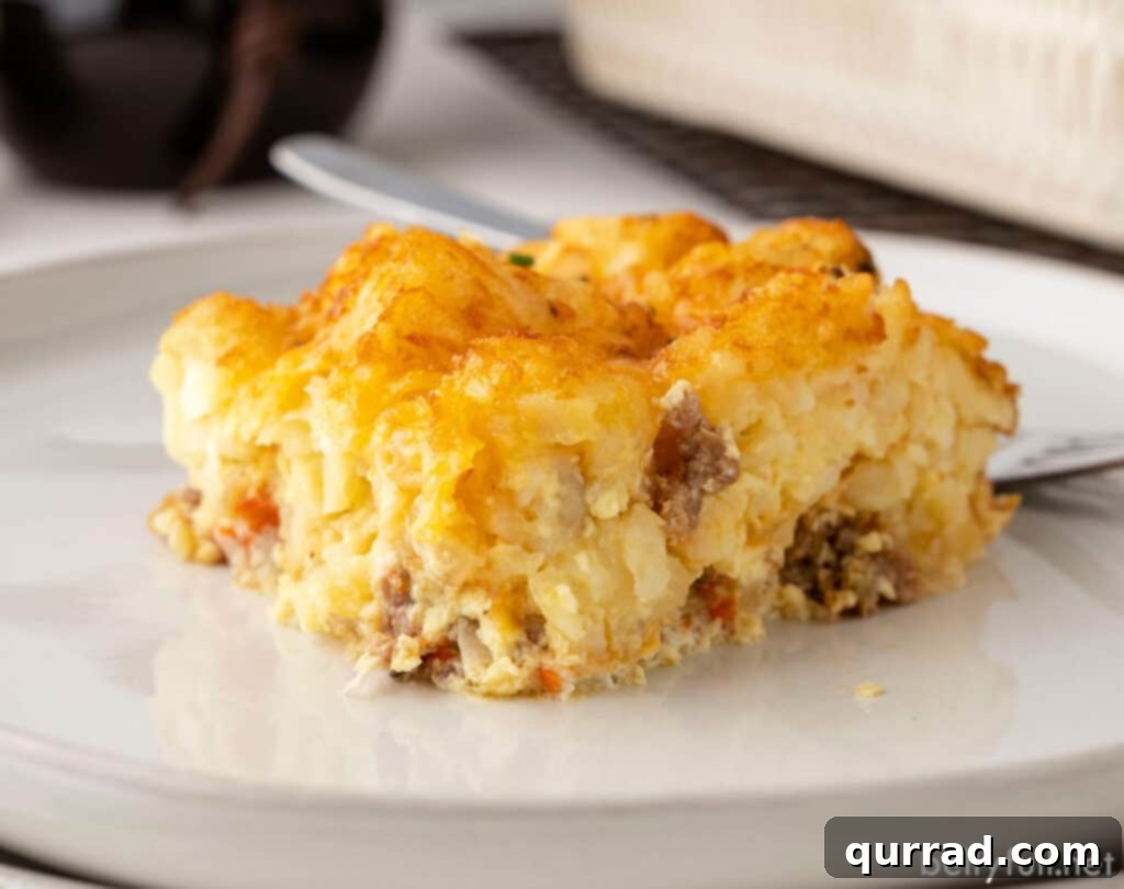 A perfectly baked slice of Tater Tot Breakfast Casserole on a white plate, showcasing its layers.